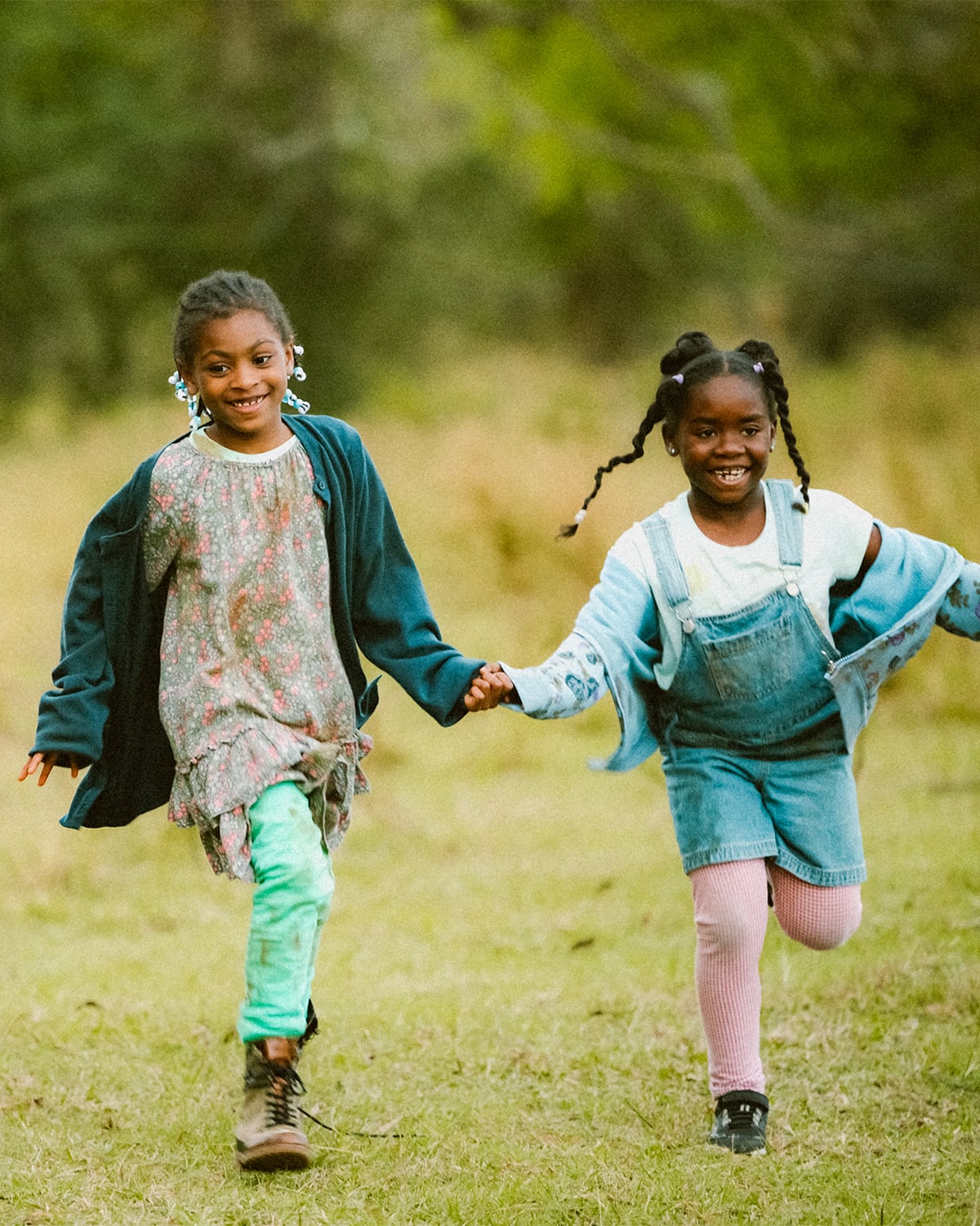 Two girls from Sound of Hope run hand in hand through a field.